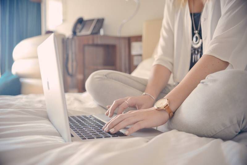 Woman sitting on bed typing on laptop - Writing about illness and injury
