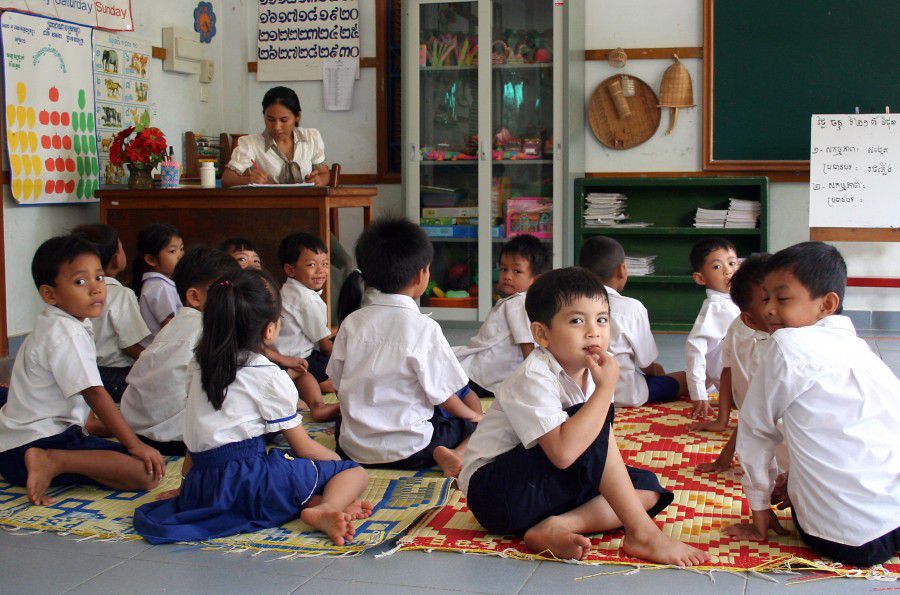 Boys and girls in school uniforms sitting on the floor in the classroom. Teacher in background. Angkor-Siem Reap. Photographer: Mr. Axel Halbhuber