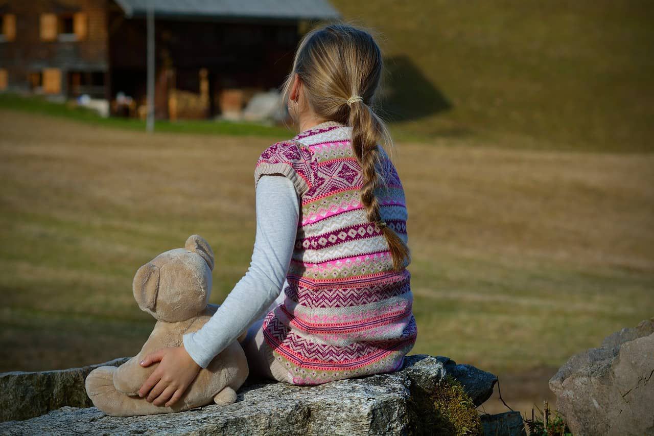 Young girl sitting alone on rock with teddy bear - A is for autism