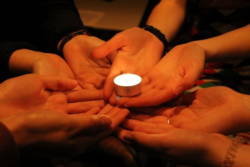 circle of hands holding candle