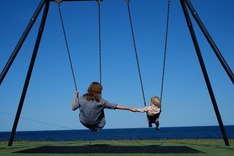 Parent and young child holding hands on swings at park - Meaningful parenting