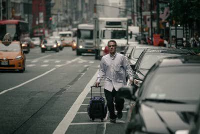 Man hurrying suitcase down busy street - The joke's on you